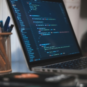 Macbook auf einem Tisch mit Code-Editor. Links steht ein Stifthalter mit verschiedenen Stiften.